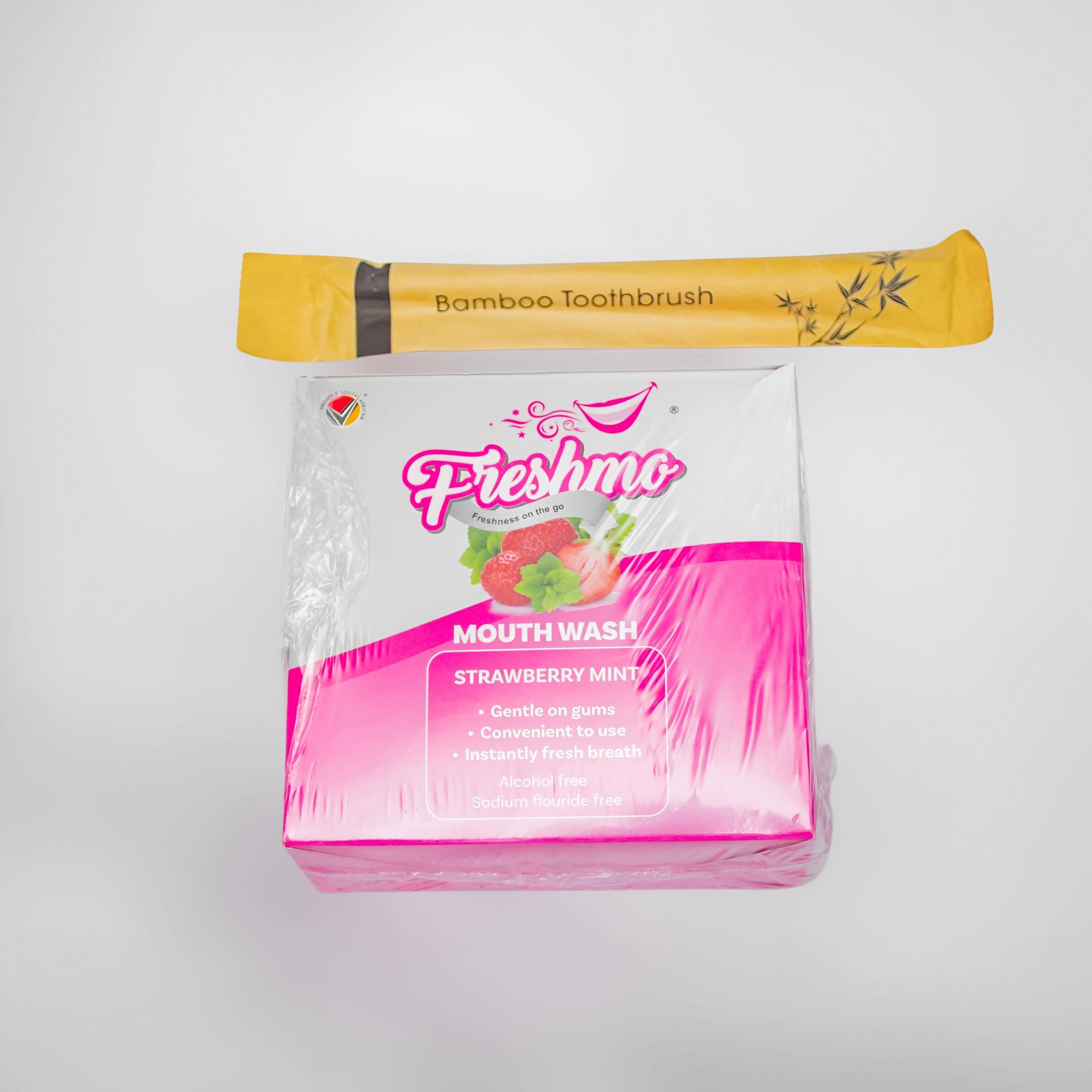 Studio flat-lay of a Freshmo bamboo toothbrush resting on the Strawberry Mint mouthwash retail box